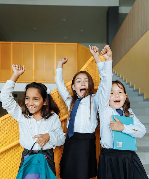 happy school children raising their hands in the air