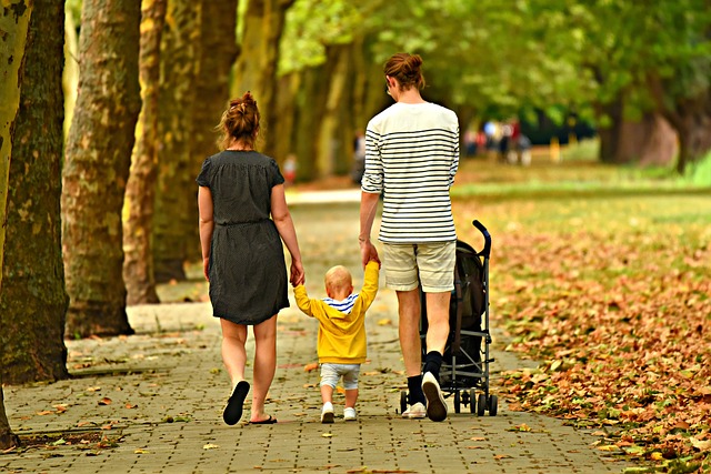 Family of three walking together in park, mother and father both holding one of their child's hands