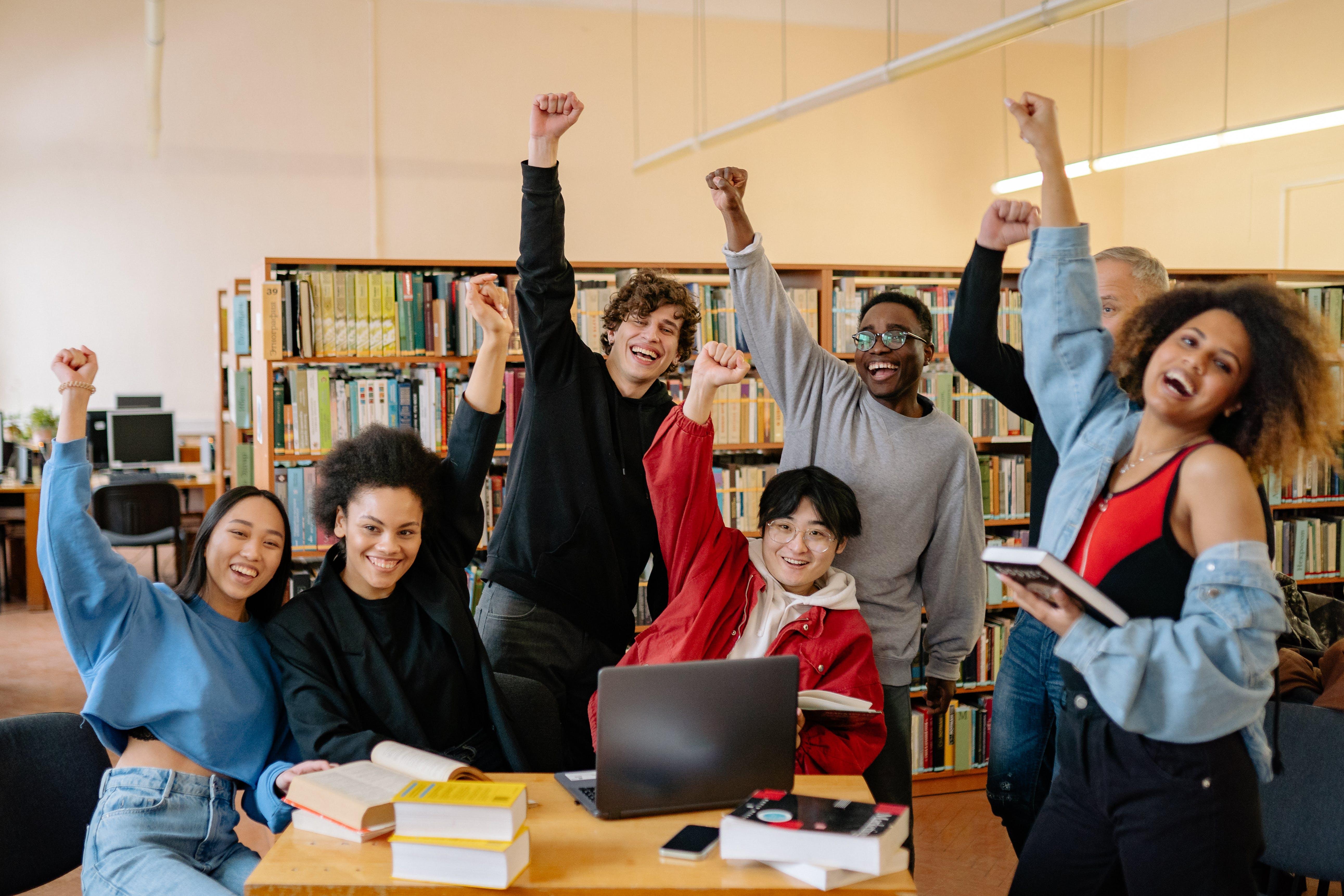 Group of students in a library raising their hands