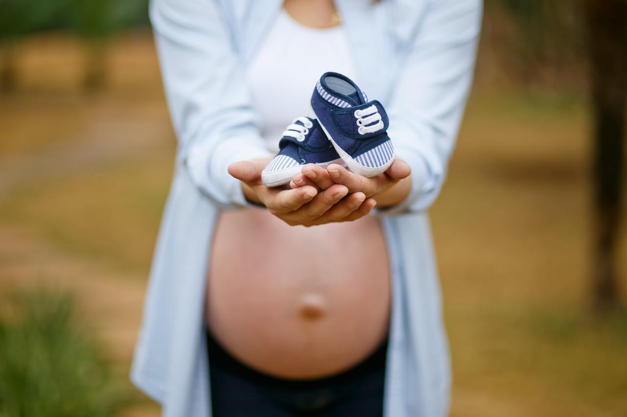 Pregnant woman holding out a pair of baby's shoes