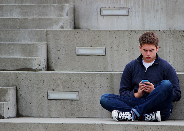 Teenager sitting alone texting on his phone